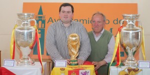 El vicario parroquial de La Palma, Karol Adam Zurav, y José Sánchez Castizo, miembro de la Federación Onubense de Fútbol, junto a los trofeos.