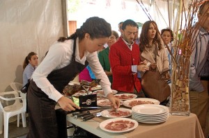 Una joven corta jamón durante el evento solidario.