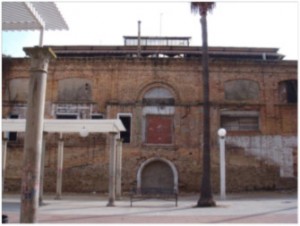 En lugar de ladrillo visto, se utiliza la pizarra en la parte baja de esta fachada porque en origen no era visible, tapada con la doble rampa para entrada de mercancías en el mercado. Los parches de alicatado, huecos cegados y otros abiertos en momentos recientes distorsionan aún más el aspecto original.