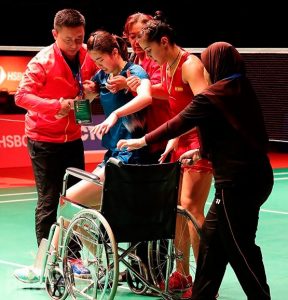 Carolina Marín ayuda a Gao a sentarse en la silla de ruedas en la que tuvo que abandonar la pista. / Foto: Badminton Photo.